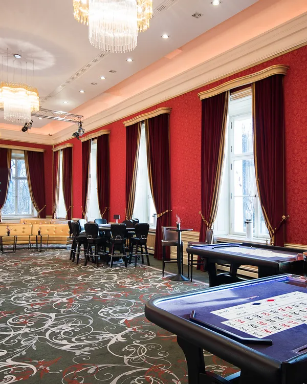 Eleganter Casino-Spielsaal mit Roulettetischen, Kronleuchtern und roten Samtvorhängen